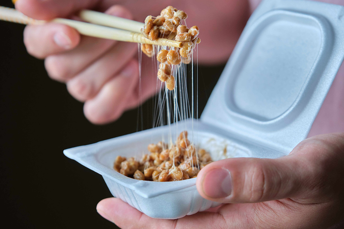 納豆を箸で持ち上げる手。納豆から糸が引いている様子が見える。