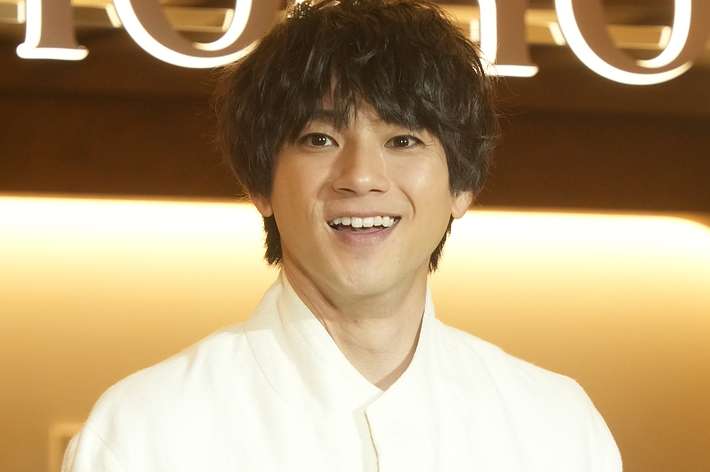 白いスーツを着た佐藤健さんが笑顔でポーズをとっている。
