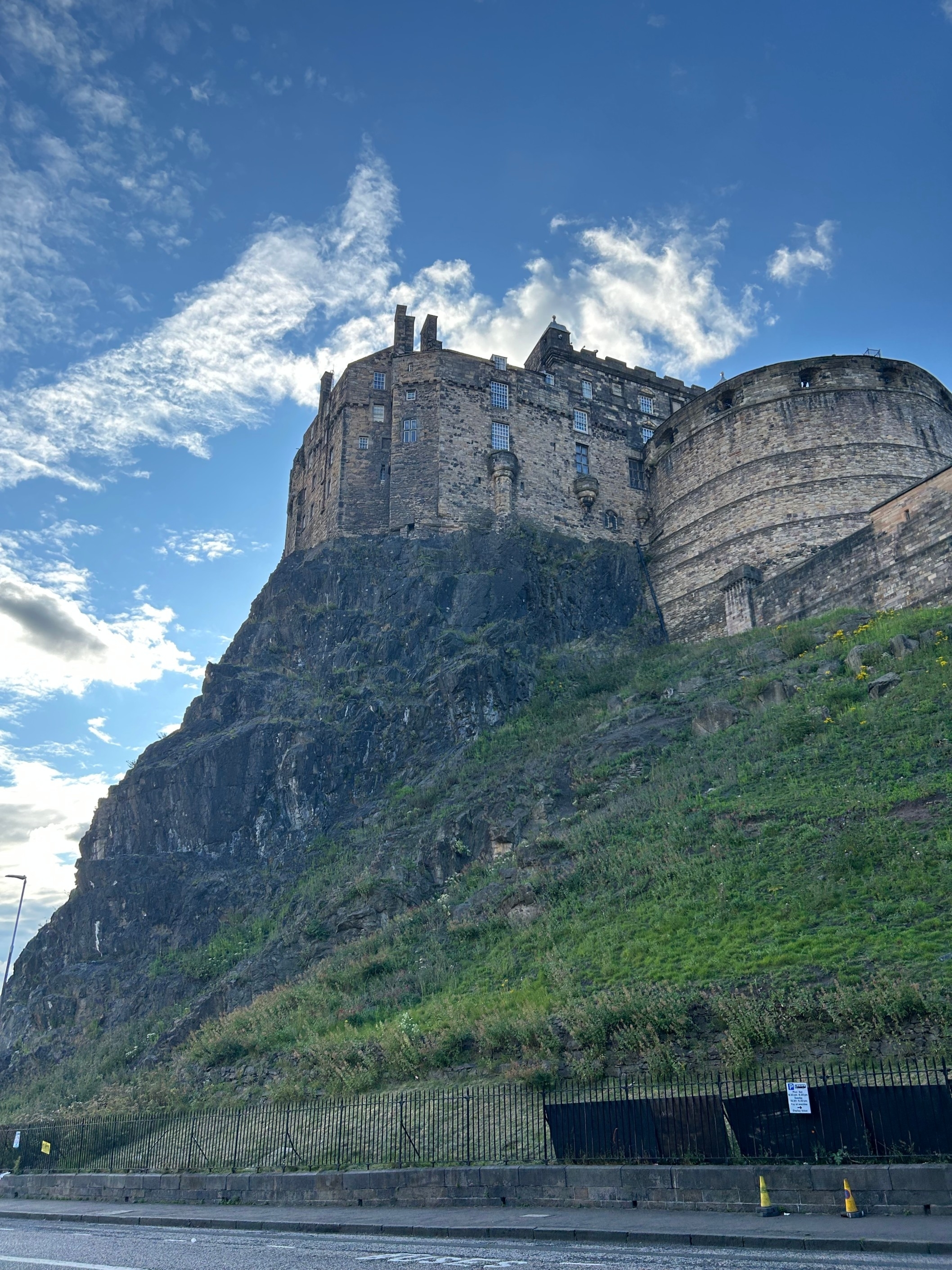 Edinburgh Castle on a hilltop with a partly cloudy sky in the background and green grass on the slopes below