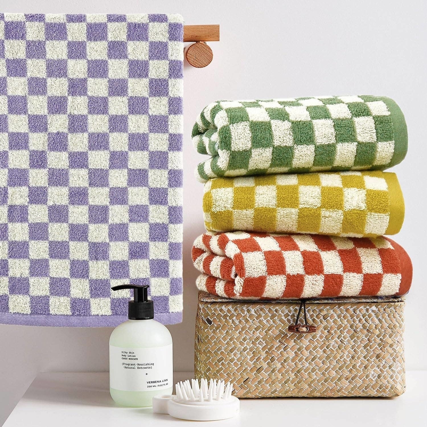 Stack of colorful checkered towels, a manus  soap bottle, brush, and wicker handbasket  displayed connected  a shelf