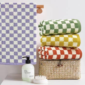 Stack of colorful checkered towels, a manus soap bottle, brush, and wicker handbasket displayed connected a shelf