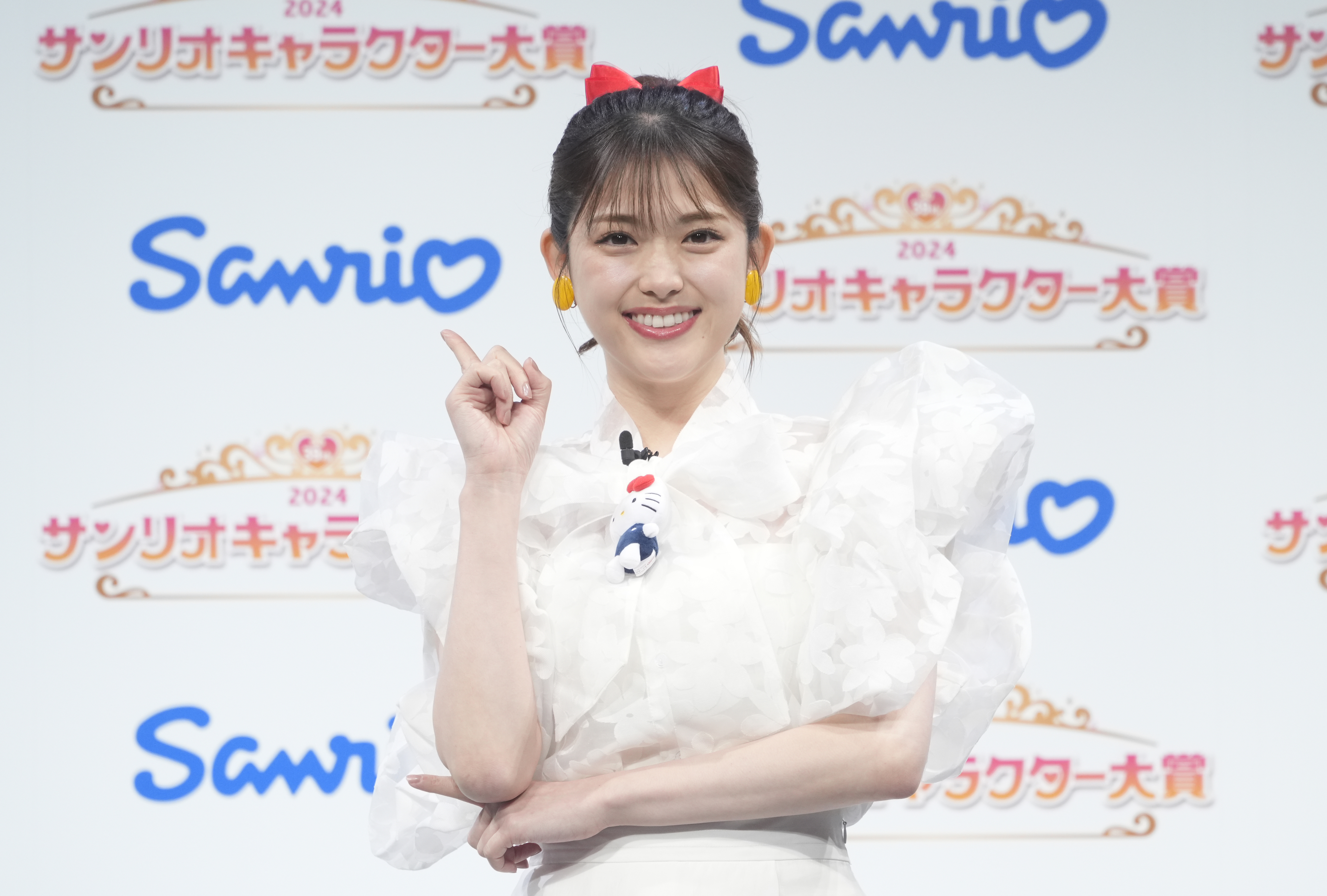 タレントの指原莉乃さんがサンリオキャラクター大賞イベントに参加し、白いドレスを着て手を指し示しています。背景には「Sanrio」と「2024」の文字。