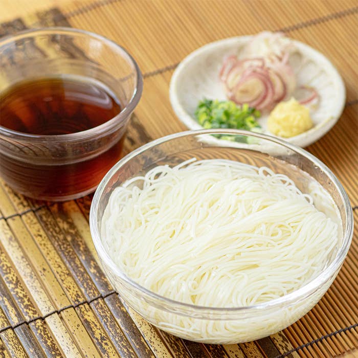 ガラスのボウルに盛られた素麺とつけだれ、薬味（ネギ、しょうが、ミョウガ）が並んだ写真。