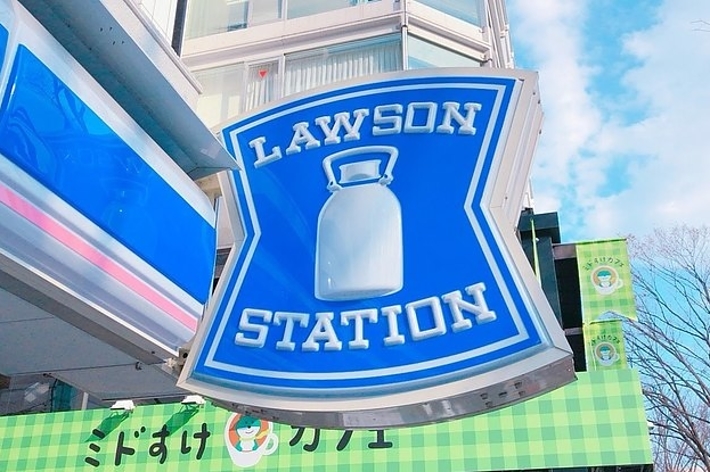 ローソンの看板。ミルク缶のロゴが中央に描かれている。背景にはビルと空が見える。