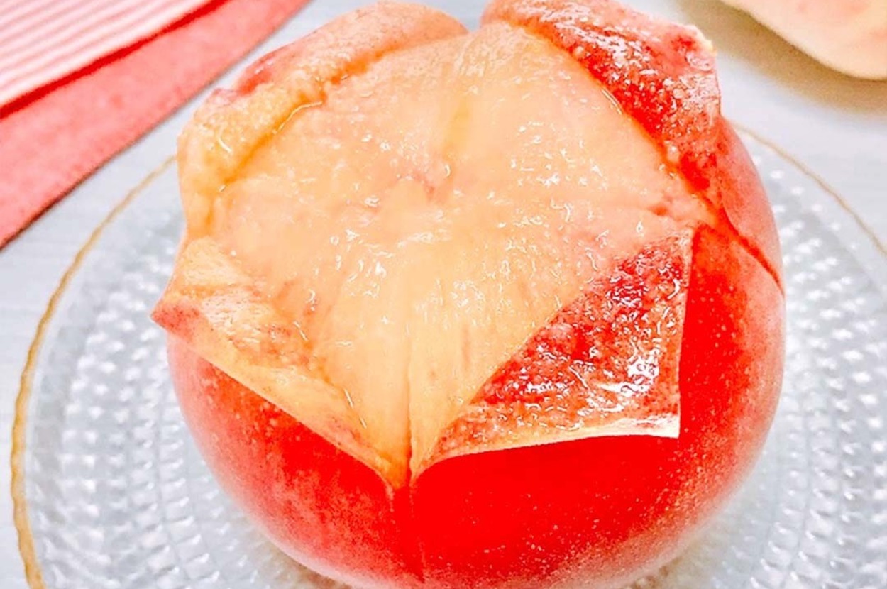 お皿に乗った熟した桃が1つ、切り目が入って皮が少し剥けています。