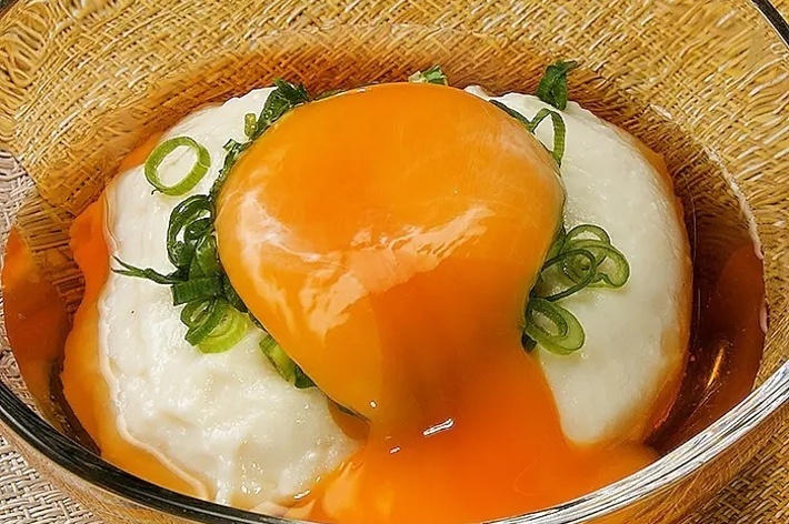ガラスの鉢に盛り付けられたポーチドエッグと緑ネギがトッピングされた豆腐料理。