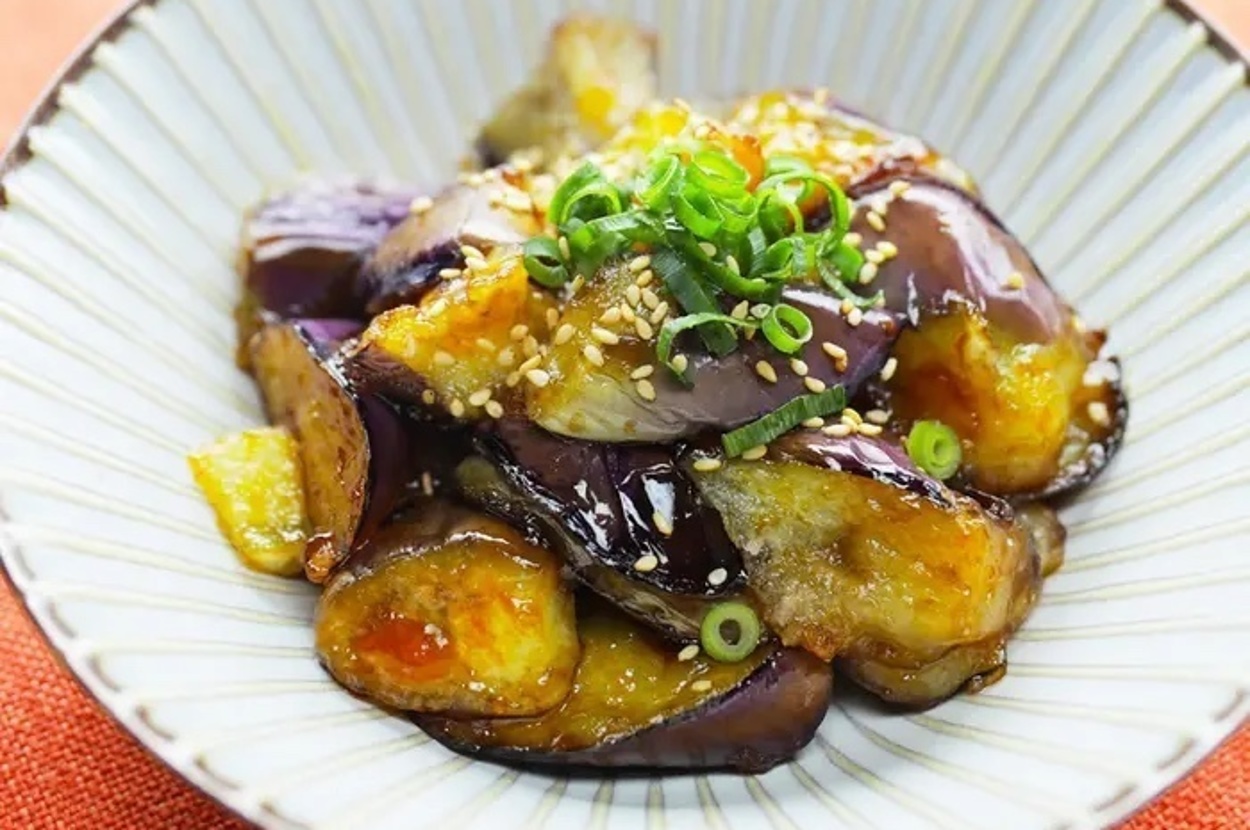 ナスの揚げびたしが小皿に盛り付けられており、ネギとゴマが上に散らされています。