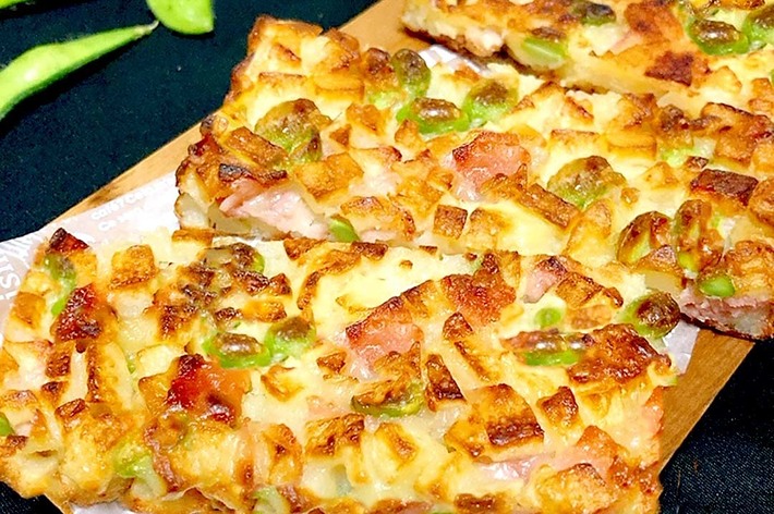 三枚の焼きたてのピザトーストが木のプレートに並べられている。横には枝豆が数本置かれている。