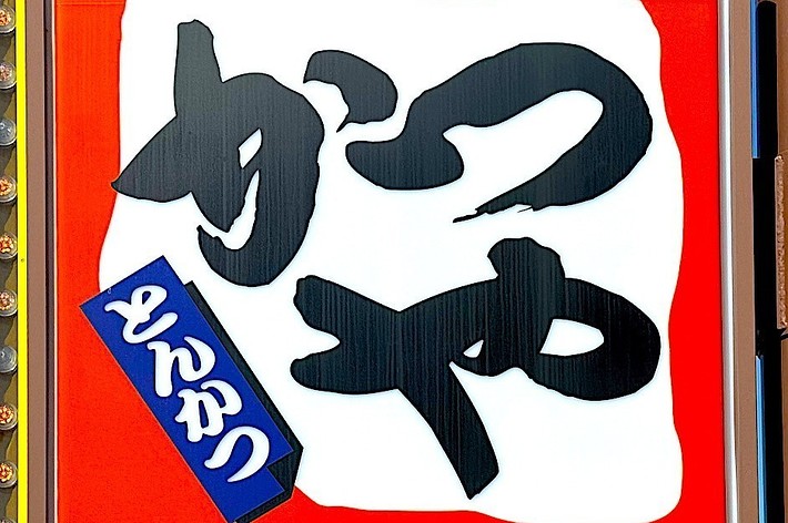 Signboard with Japanese text, including the characters &ldquo;かつや&rdquo; and &ldquo;とんかつ,&rdquo; indicating a restaurant specializing in pork cutlets