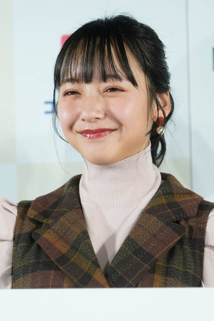 若月佑美さんが笑顔で写っている画像。彼女は淡い色のハイネックのトップスにチェック柄のジャケットを着ています。