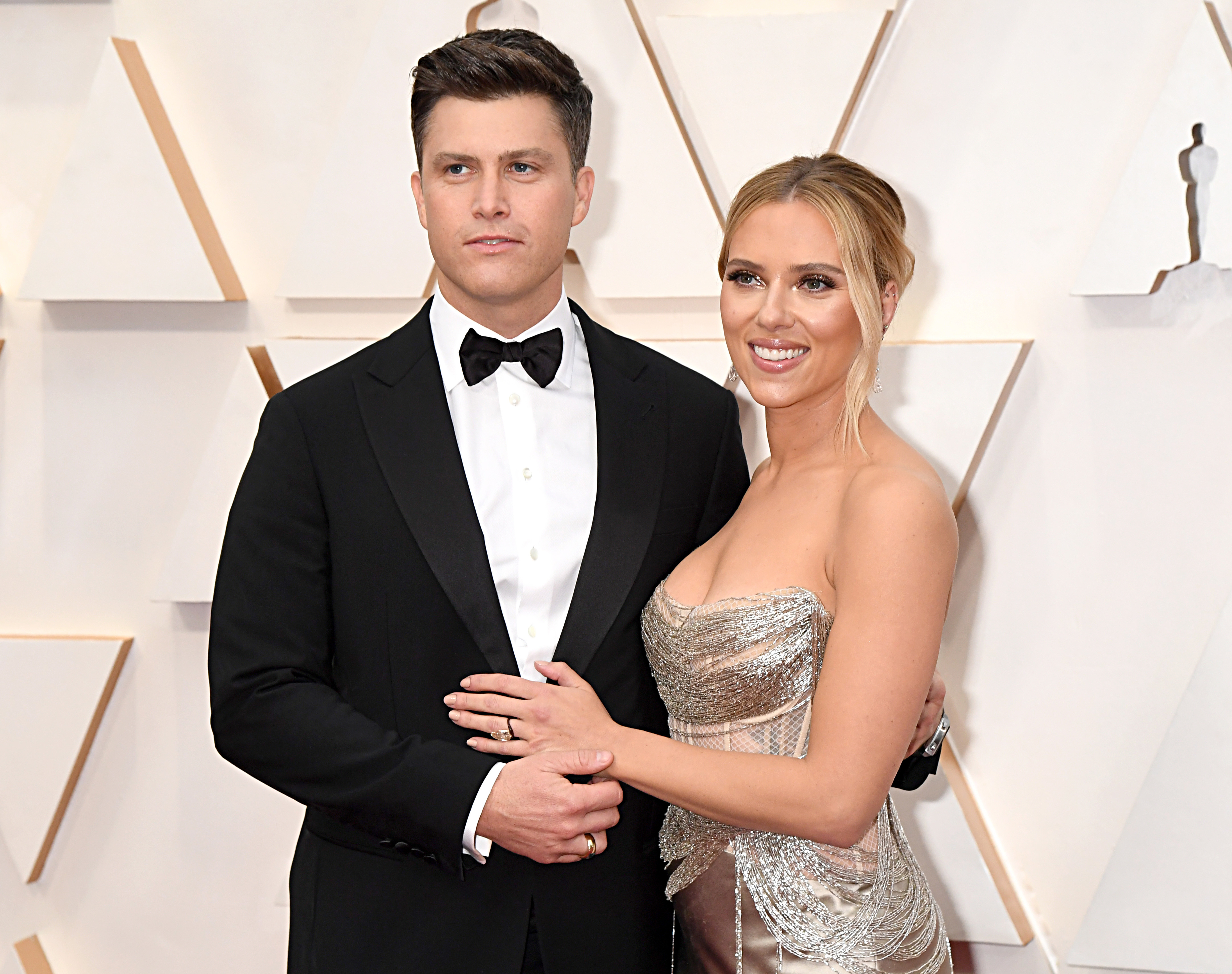 Scarlett Johansson in a strapless gown and Colin Jost in a black tuxedo smiling, pose together on a red carpet event