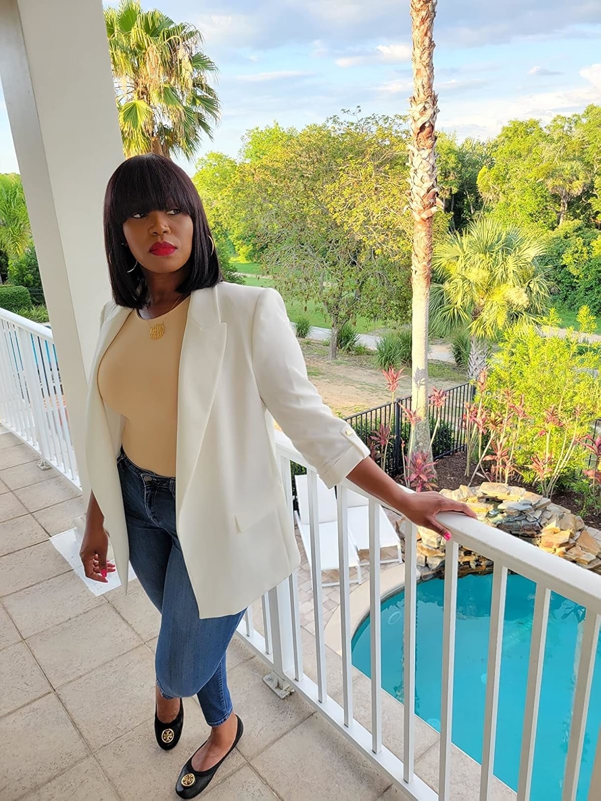 reviewer wearing a achromatic  blazer, beige bodysuit, bluish  jeans, and achromatic  flats lasting  connected  a balcony