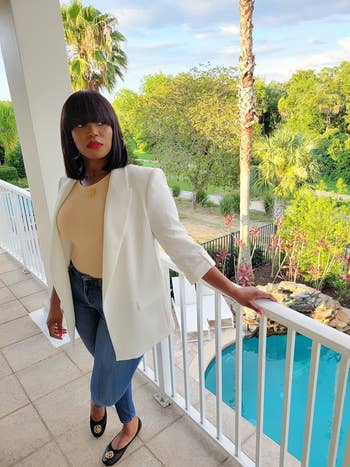 reviewer wearing a achromatic blazer, beige bodysuit, bluish jeans, and achromatic flats lasting connected a balcony