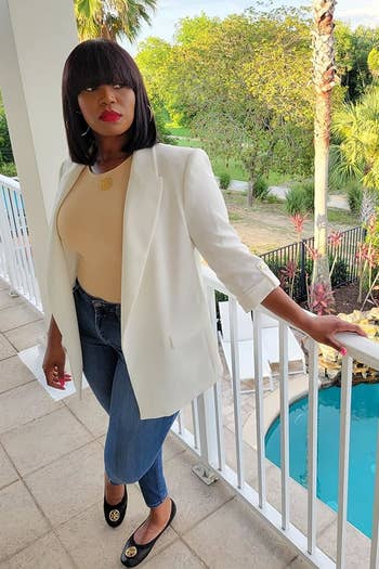 reviewer wearing a achromatic blazer, beige bodysuit, bluish jeans, and achromatic flats lasting connected a balcony