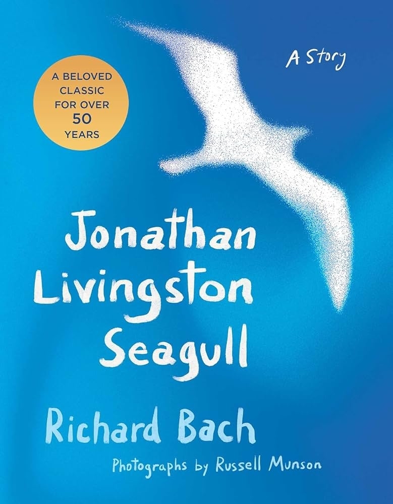 Cover of the book "Jonathan Livingston Seagull" by Richard Bach, with a seagull silhouette and text highlighting it as a beloved classic for over 50 years. Photographs by Russell Munson