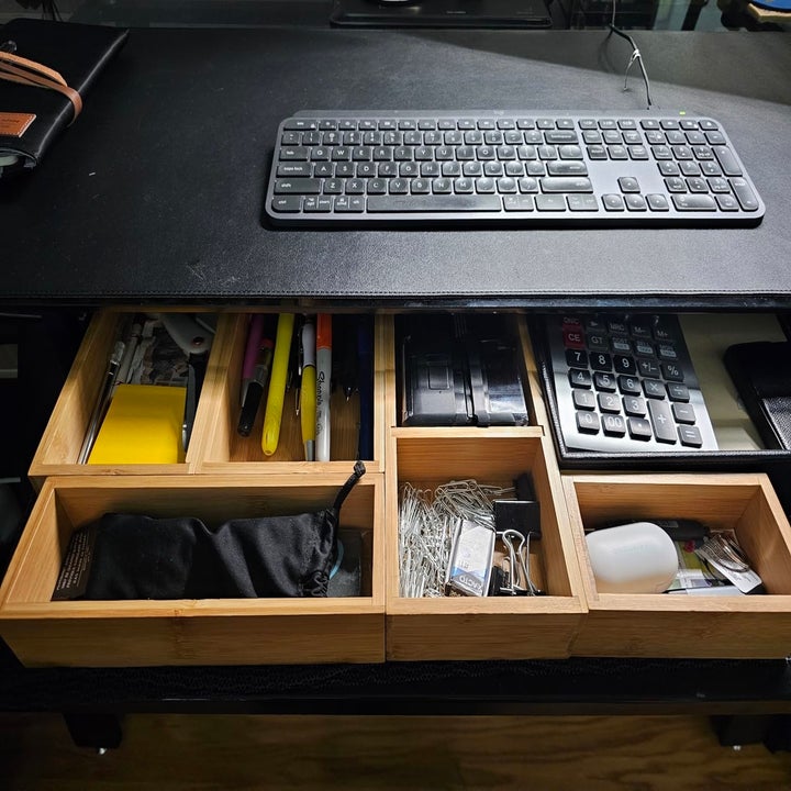 An organized desk drawer with bamboo dividers holds various office supplies, including pens, highlighters, a calculator, a keyboard, and miscellaneous items