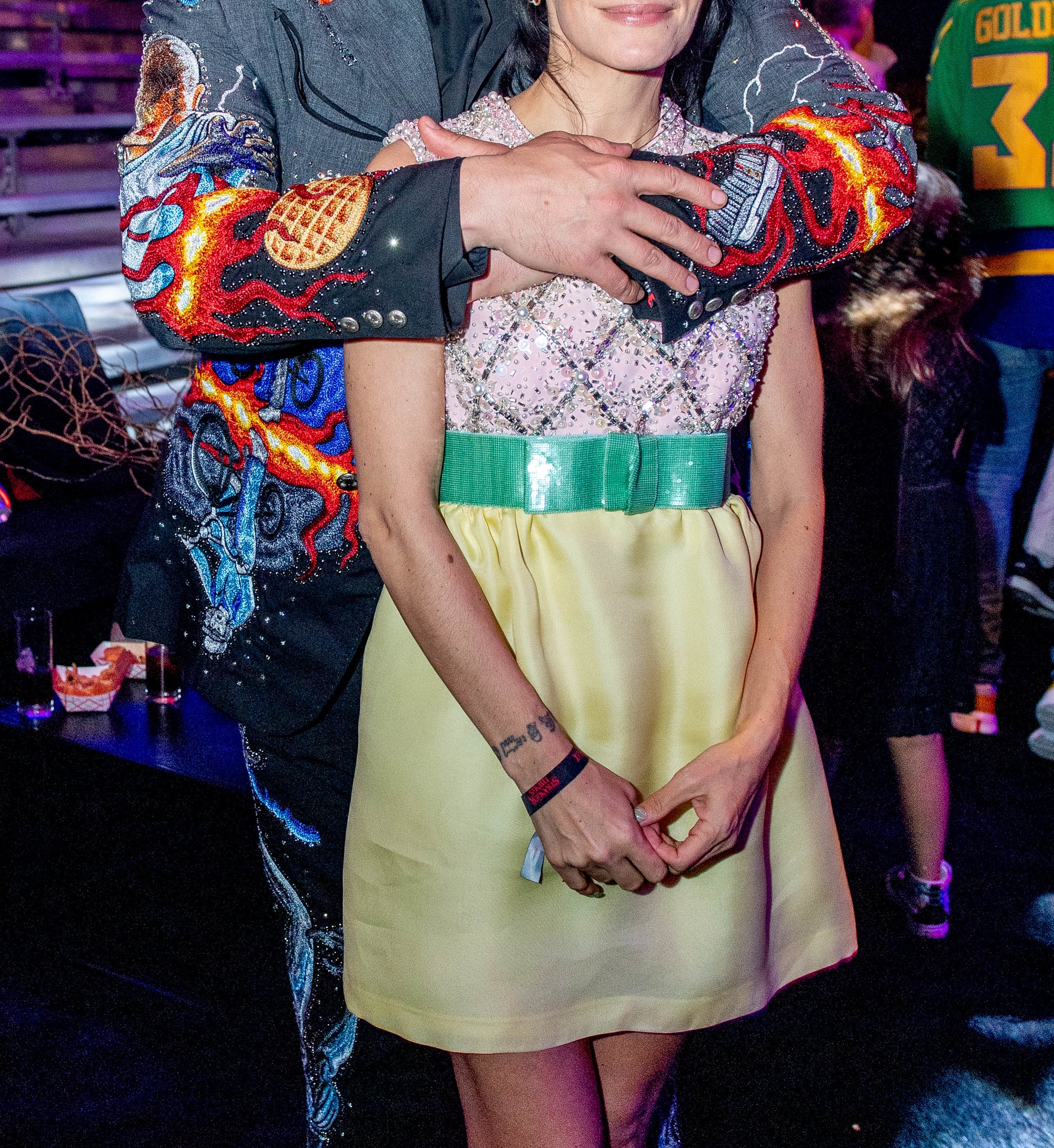 David Harbour and Lily Allen pose together at an event. David is wearing a colorful, embroidered jacket and Lily is in a short dress with a patterned top and light skirt