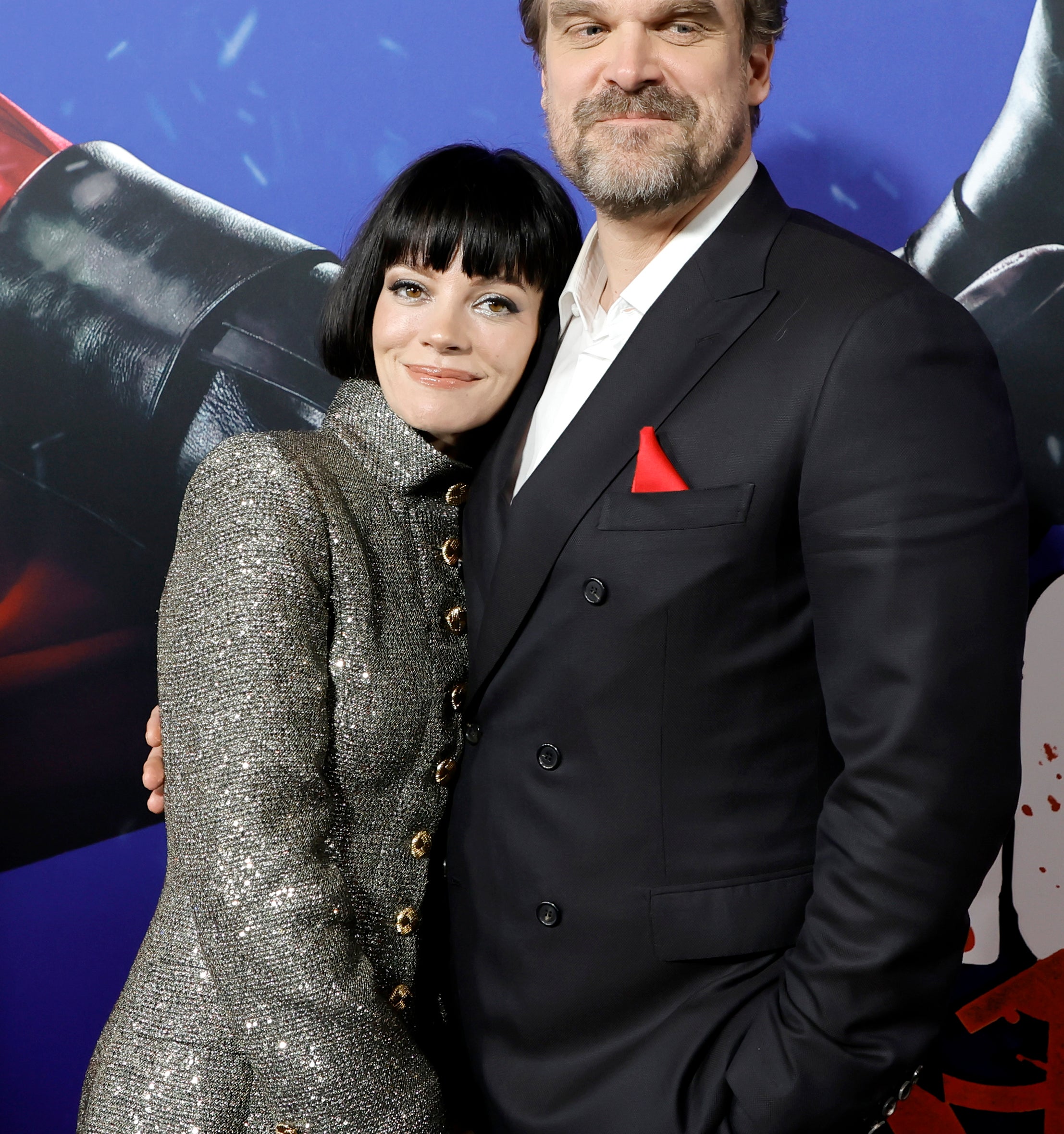 Lily Allen, in a textured coat with large buttons, and David Harbour, in a dark suit with a red pocket square, pose together at a media event