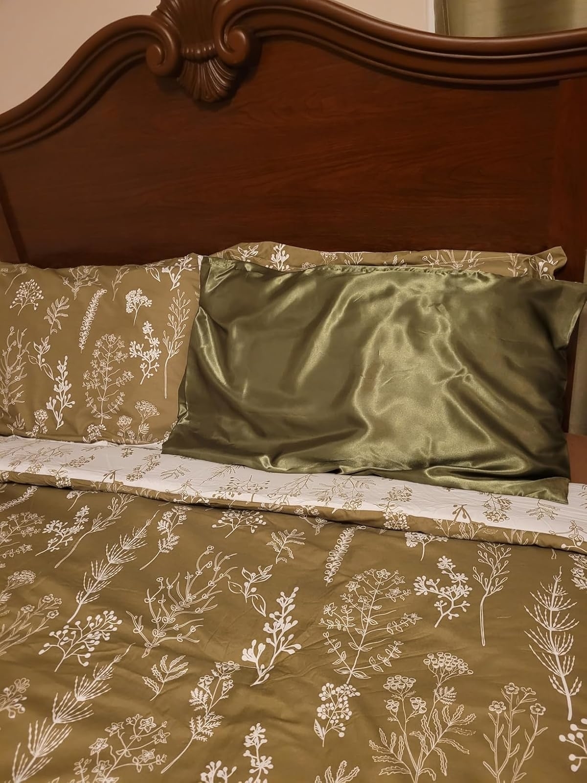 A bed with a green floral-patterned comforter and matching pillowcases, along with a silk pillow on a wooden headboard