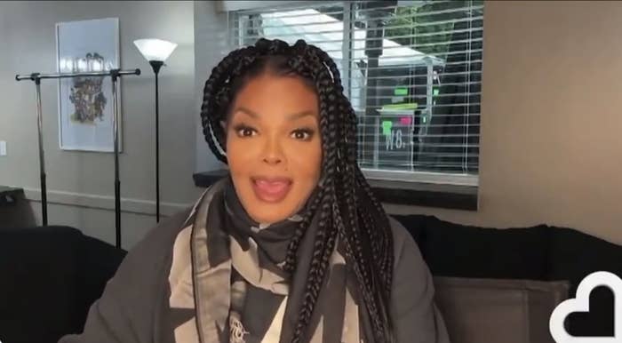 Janet Jackson seated indoors, smiling, with long braided hair and wearing a patterned scarf