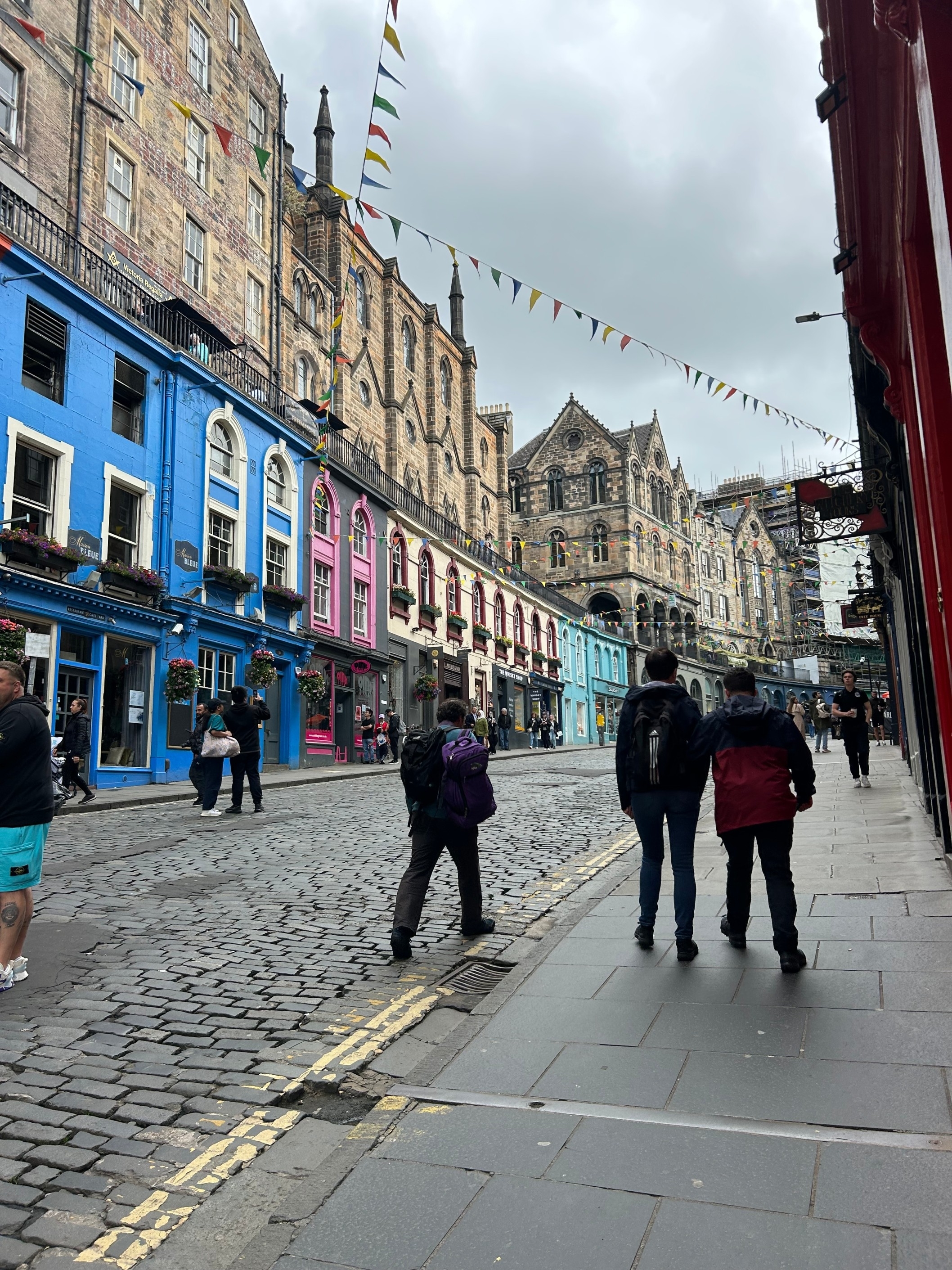 Three people walk on a cobblestone street lined with colorful buildings and bunting