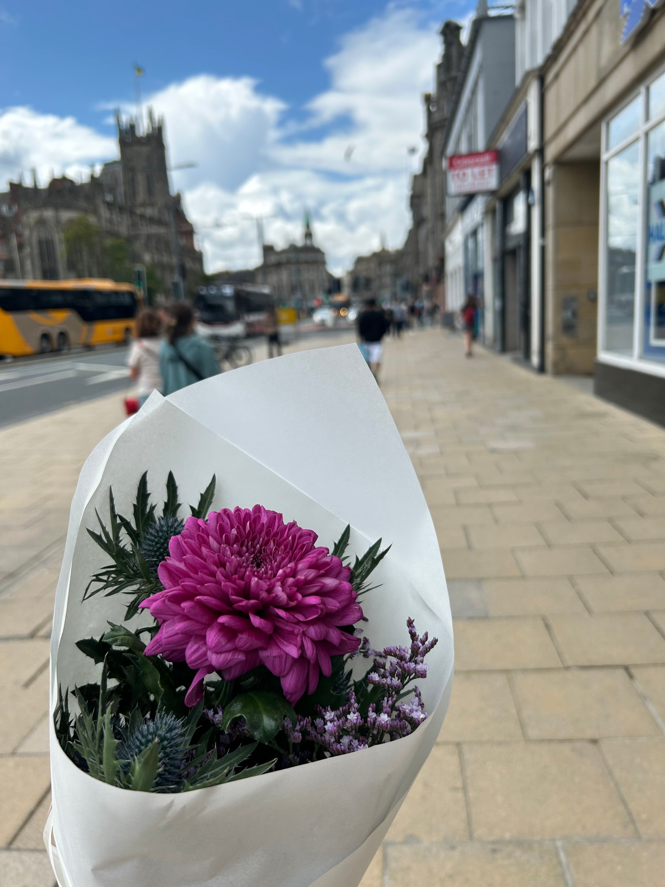 A bouquet of flowers held on a sidewalk next to a bustling city street with historical buildings in the background