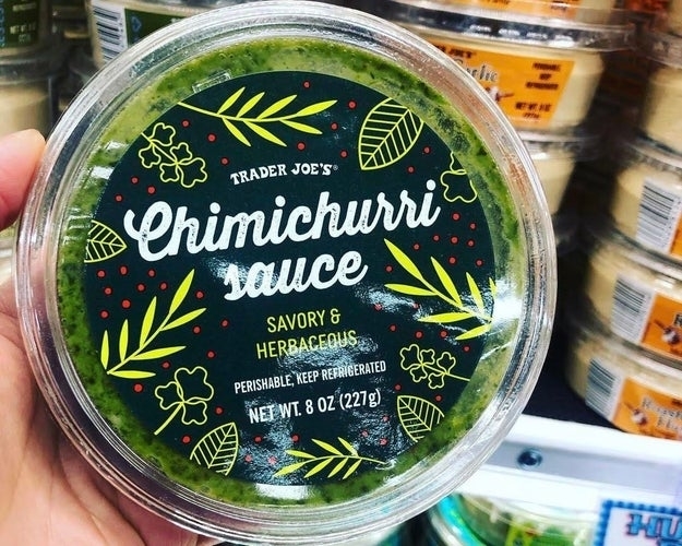 Container of Trader Joe's Chimichurri Sauce held in hand, labeled &quot;Savory &amp;amp; Herbaceous, Perishable, Keep Refrigerated, Net Wt 8 OZ (227 g).&quot;