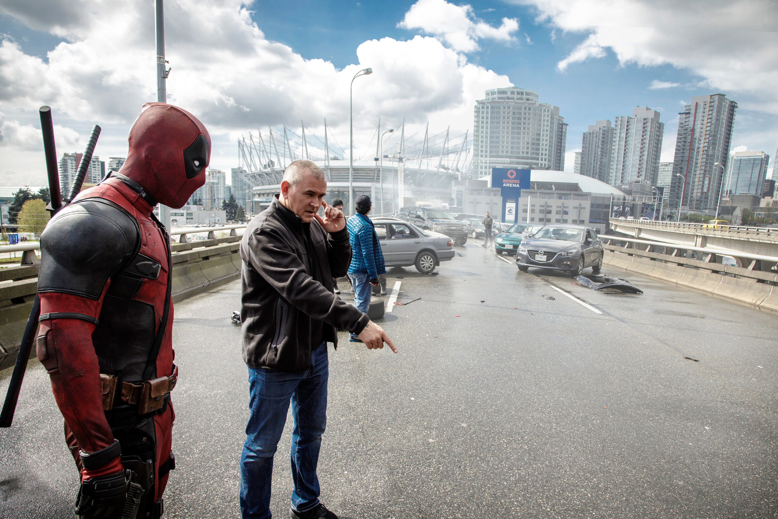 Ryan Reynolds in Deadpool costume and director Tim Miller on a highway set with crashed cars in the background, filming a scene for the movie Deadpool