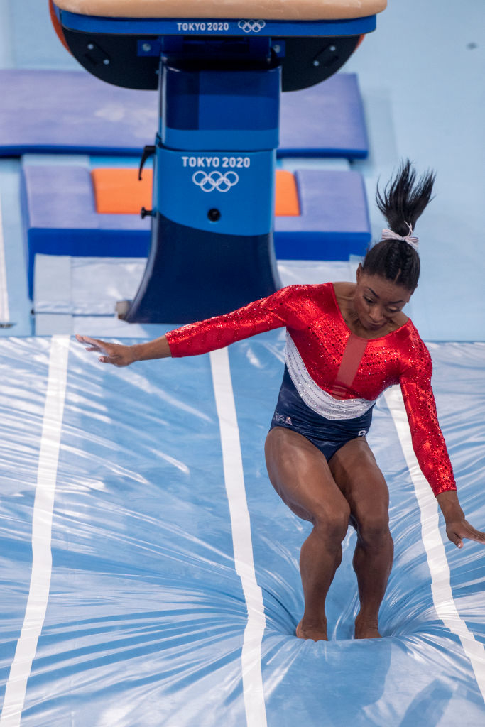 Simone Biles landing during a gymnastics event at the Tokyo 2020 Olympics, wearing a sparkling red and white leotard