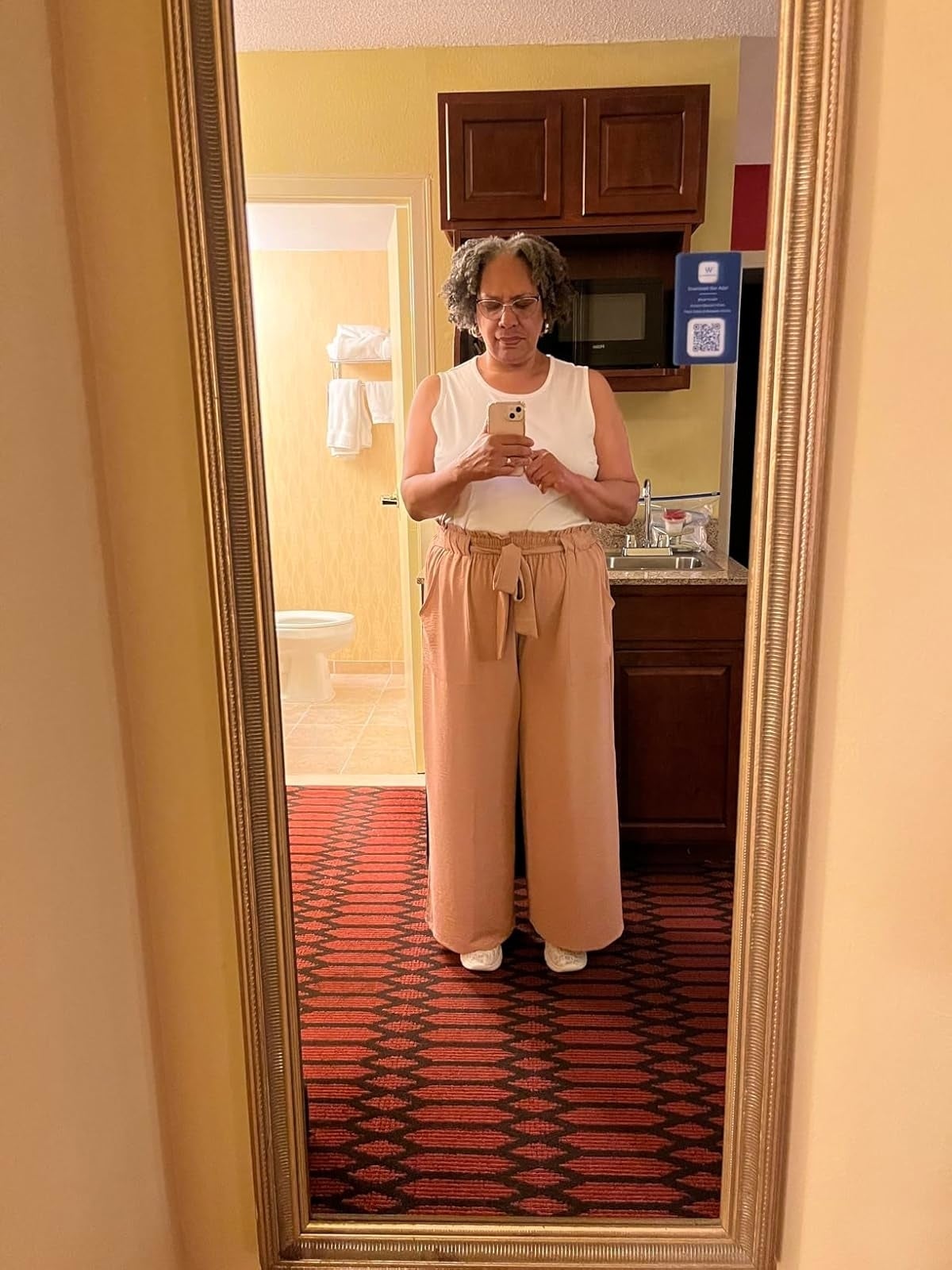 A reviewer takes a full-length reflector  selfie successful  a bathroom. She wears a achromatic  sleeveless top, high-waisted wide-leg pants with a belt, and achromatic  shoes