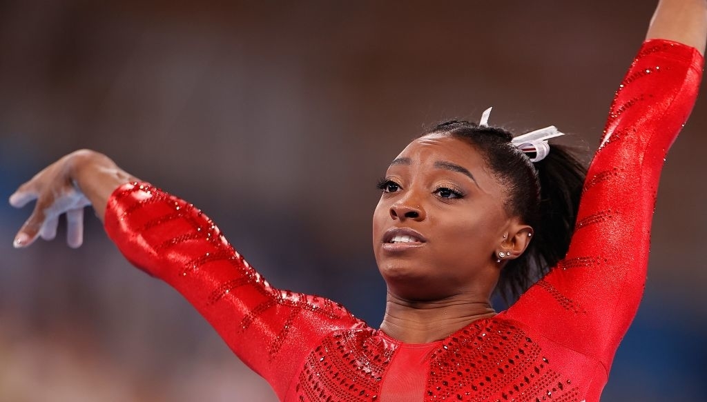 Simone Biles performs a gymnastics routine, wearing a sparkly leotard with outstretched arms