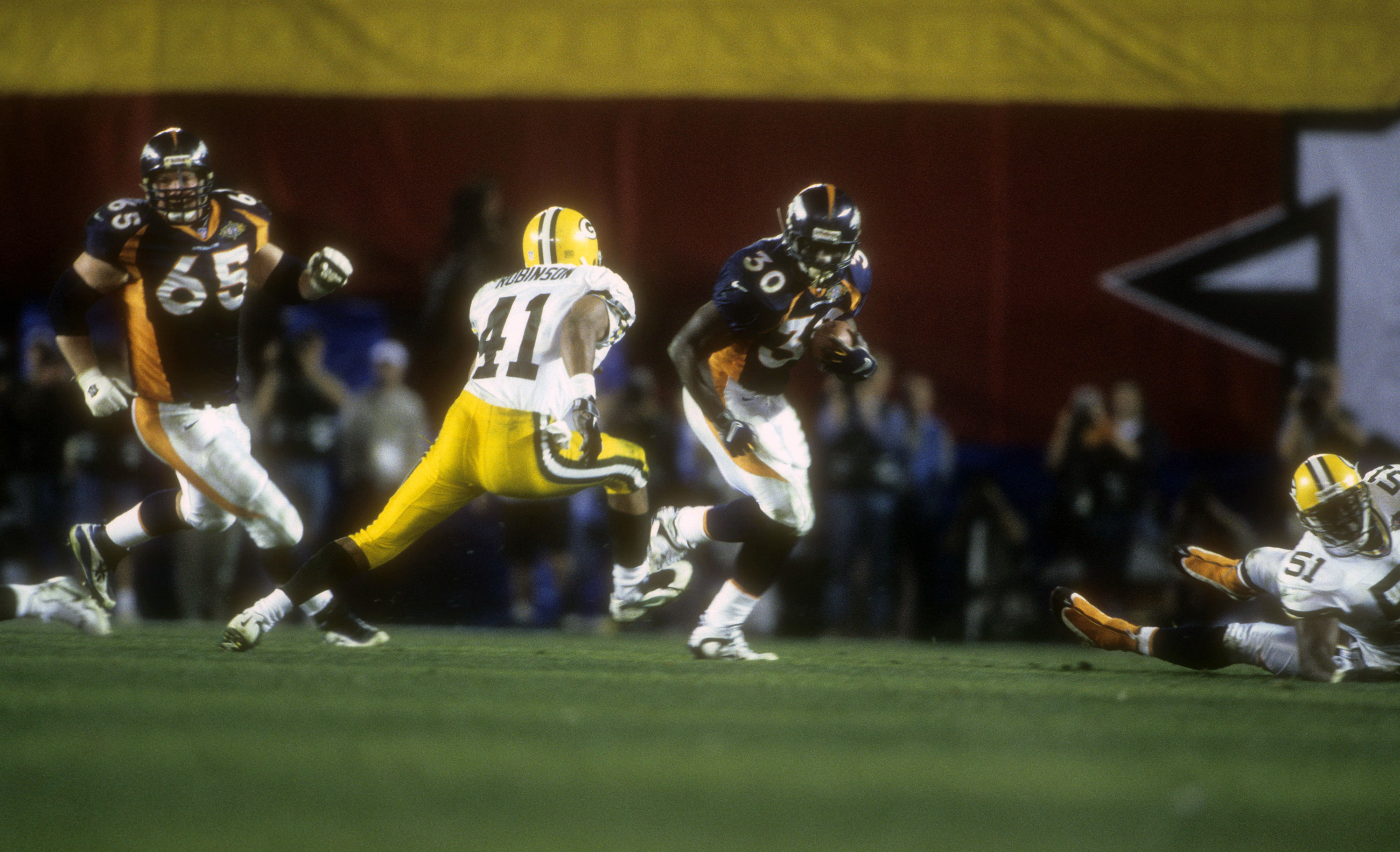 Football game action shot showing Denver Broncos player Terrell Davis running the ball while Green Bay Packers players Eugene Robinson and Bernardo Harris chase