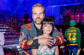 David Harbour and Lily Allen pose together at an event. David is wearing a colorful, embroidered jacket and Lily is in a short dress with a patterned top and light skirt