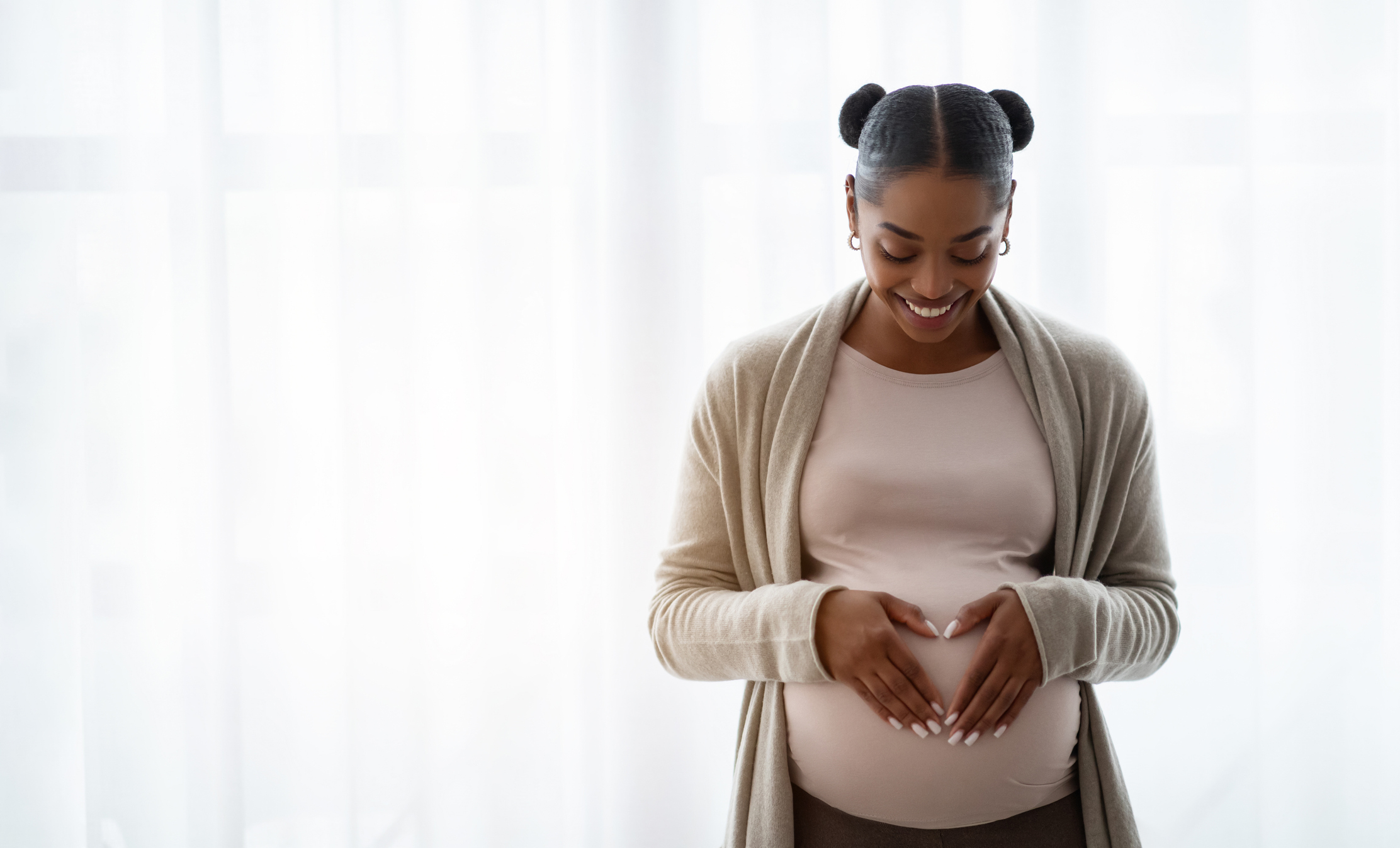 Pregnant woman smiles while cradling her belly with both hands, forming a heart