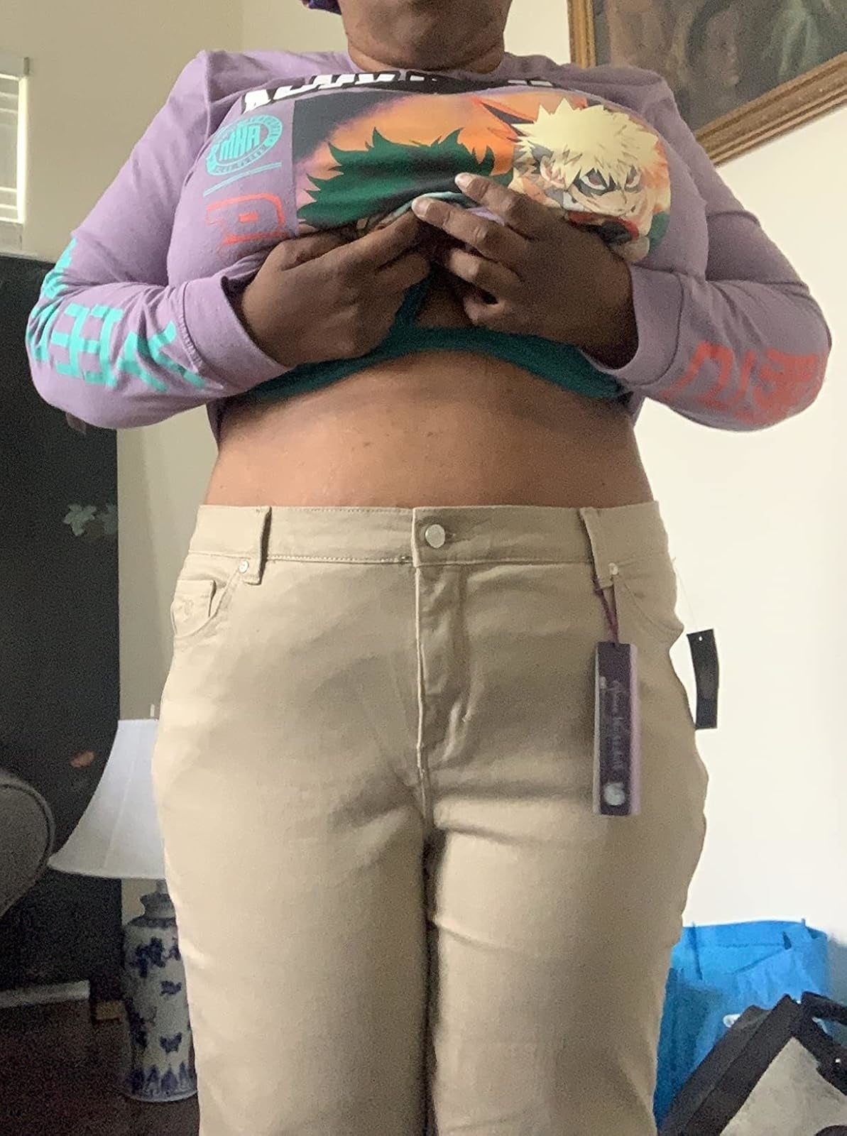 Person wearing beige pants and a purple anime-themed long-sleeve shirt, holding up   the garment  to amusement   however  pants fit