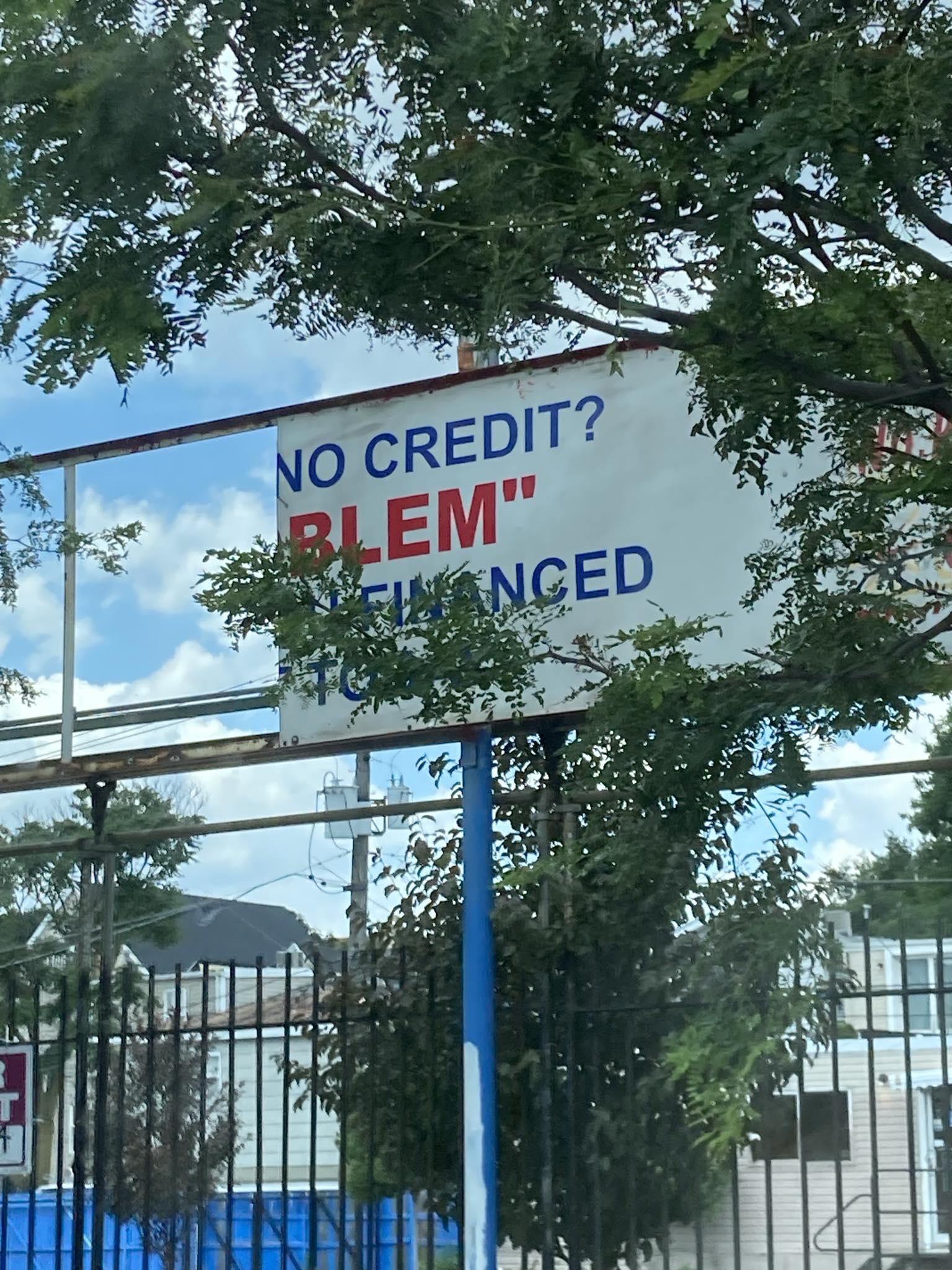 Billboard partially obscured by trees reads, "NO CREDIT? BLEMIENCED."