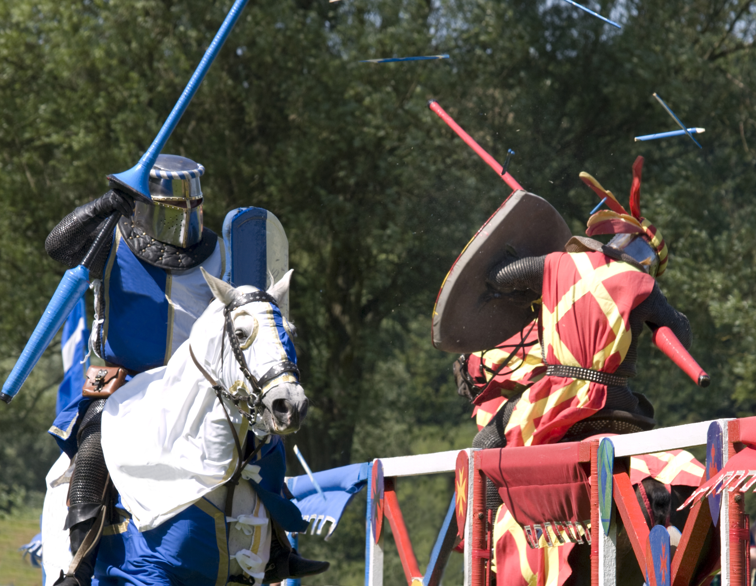 Two knights on horseback jousting. The knight on the left wears blue armor, and the one on the right wears red and gold armor