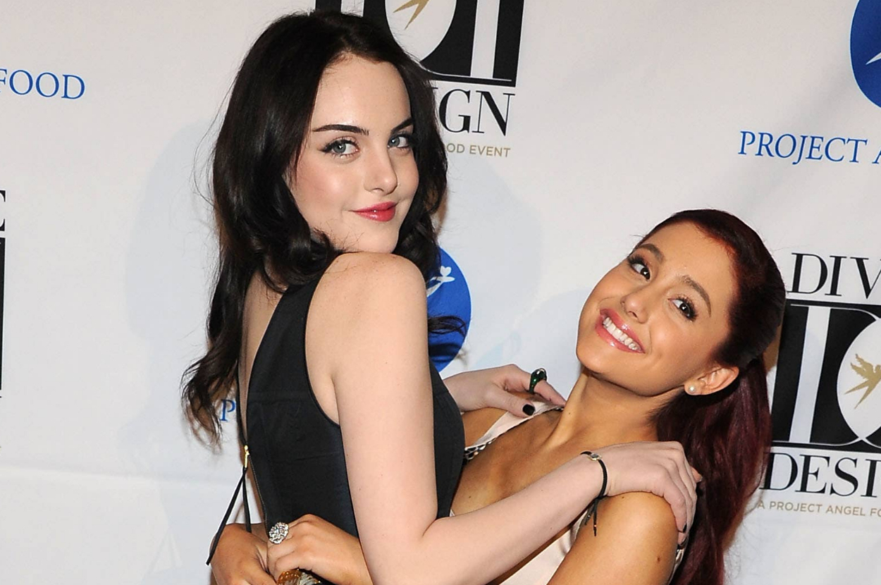 Elizabeth Gillies in a black dress and Ariana Grande in a dress, smiling and embracing on the red carpet at a Project Angel Food event