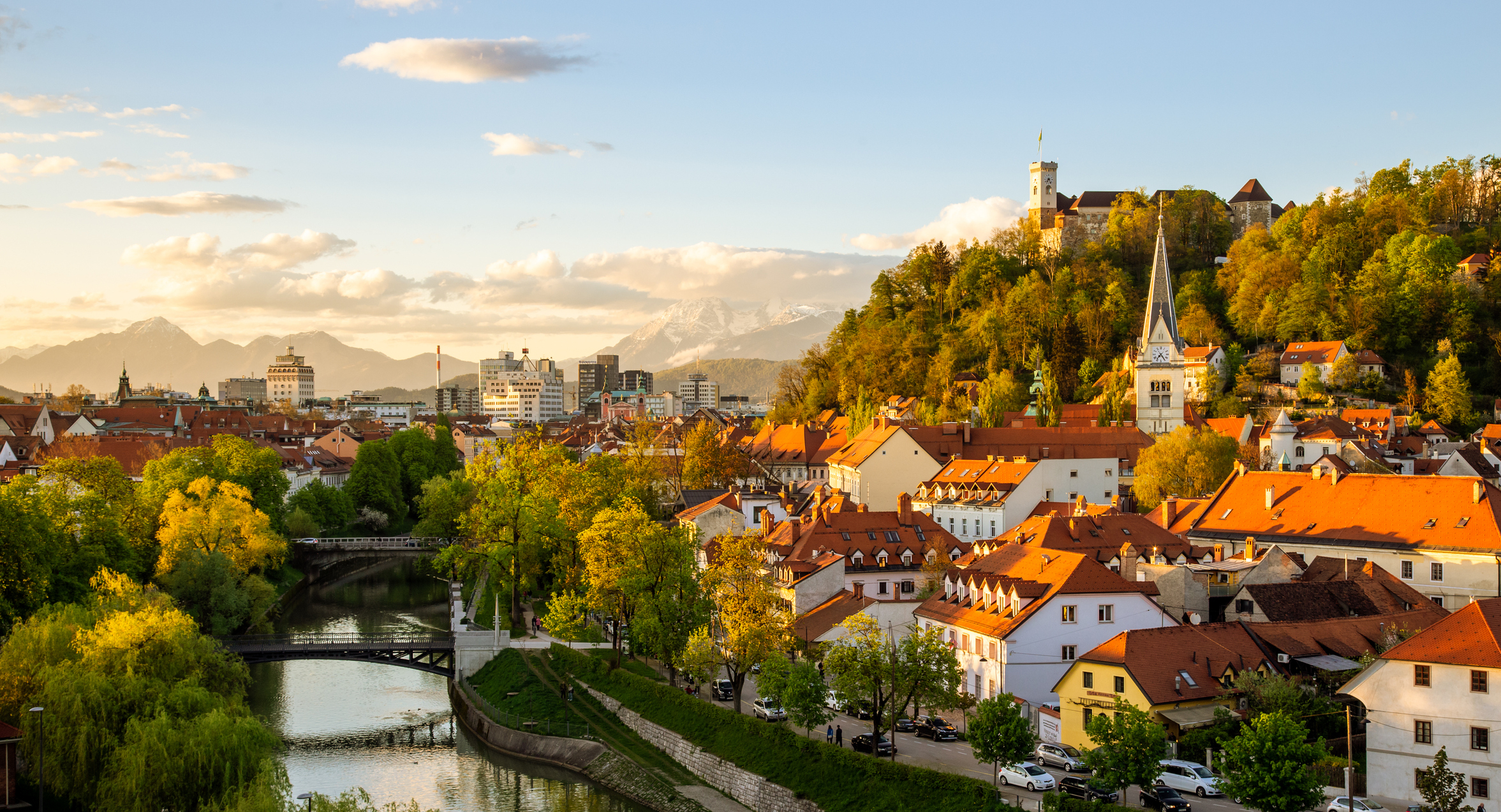 Scenic view of Ljubljana, Slovenia, featuring the Ljubljanica River, Ljubljana Castle on a hill, and a mix of historical and modern buildings