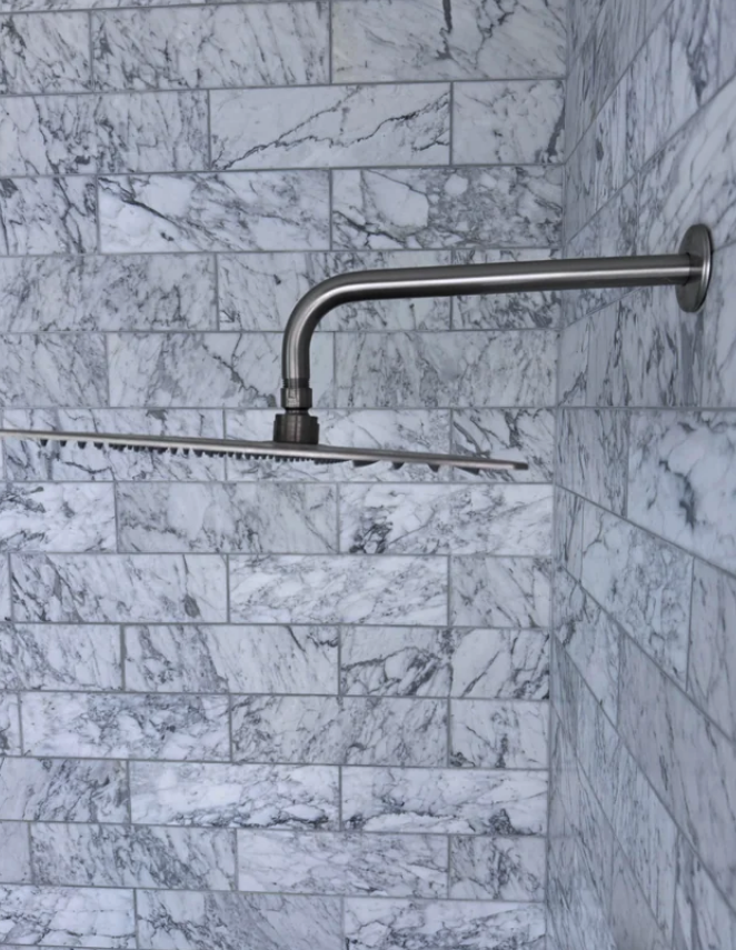 Modern design shower with a sleek metallic showerhead mounted on a marble tiled wall