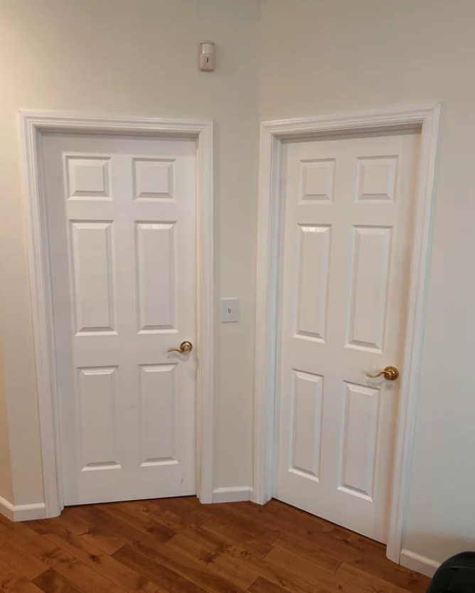 Two white, six-panel interior doors with gold handles stand side by side on a hardwood floor inside a home