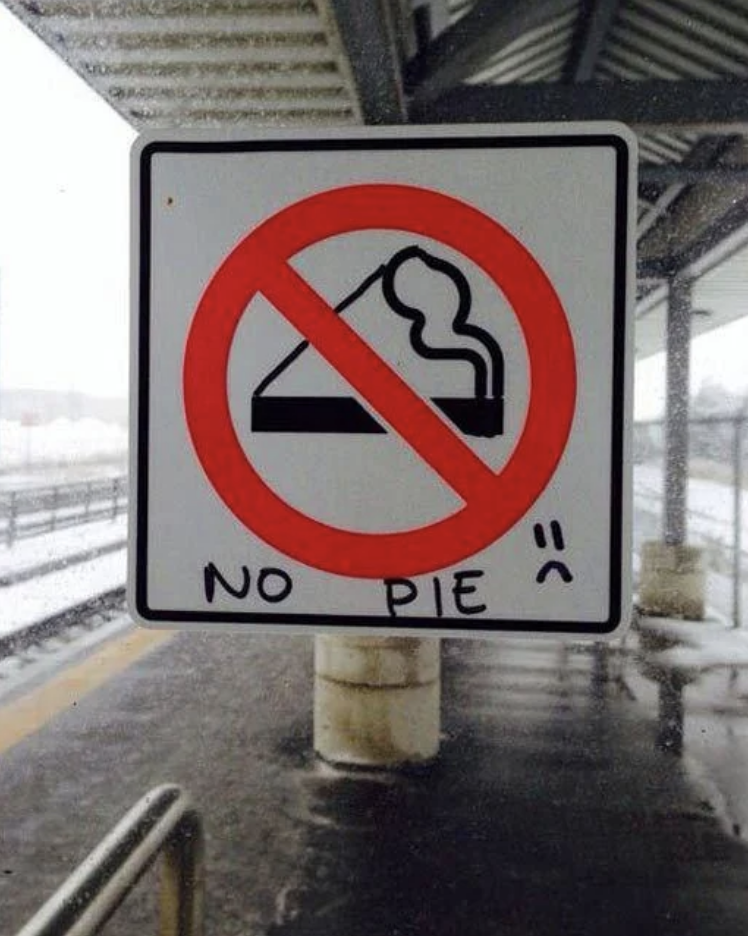 Sign showing a crossed-out pie slice with a caption "NO PIE" and a sad face below, located at a snowy train station