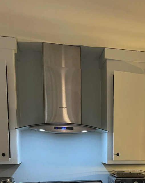 Stainless steel kitchen range hood with a digital display, installed between two white cabinets