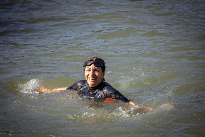 Woman in a wetsuit and goggles smiles while floating in a body of water