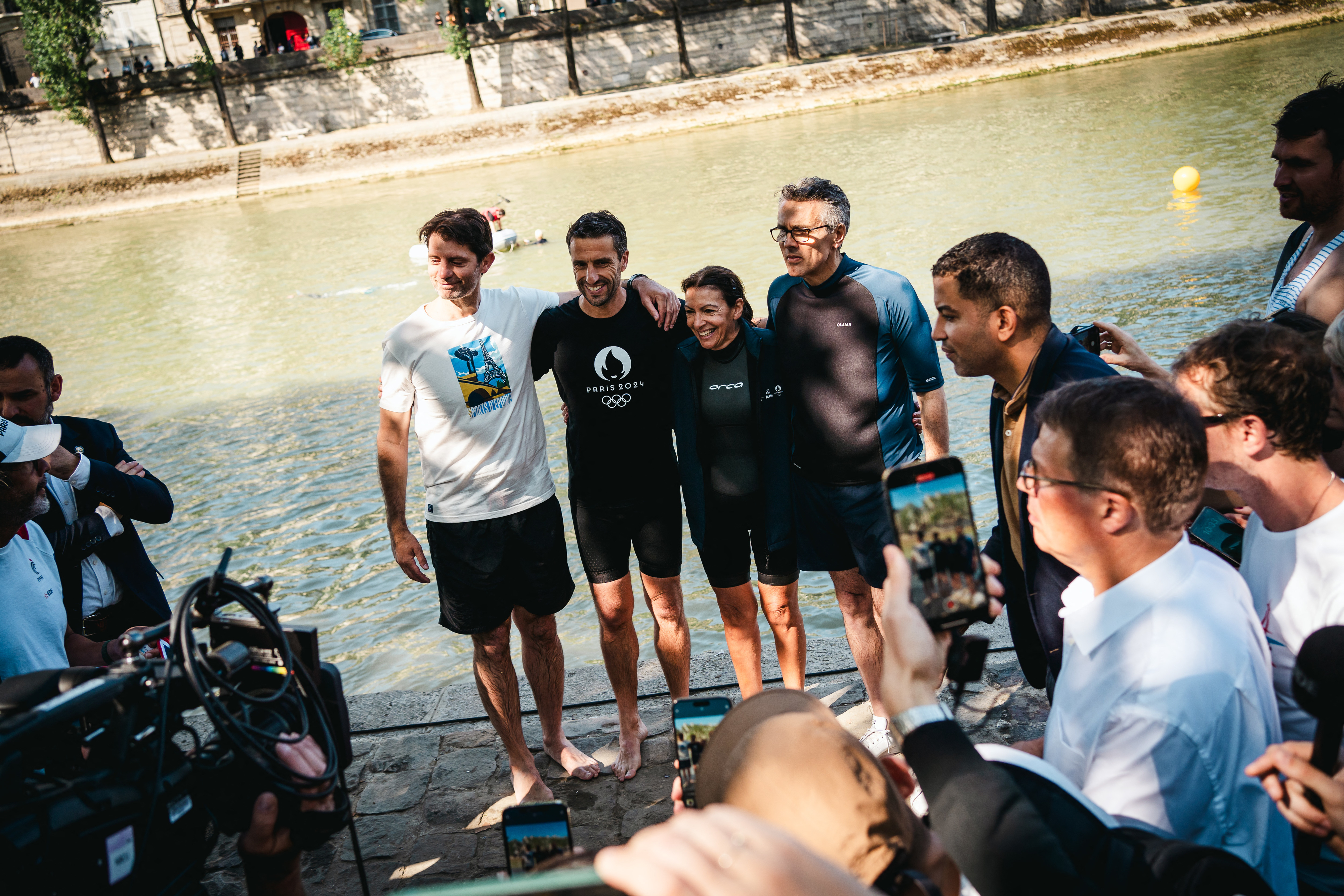 I don't know who they are. Group of four people in athletic wear by a river, surrounded by media personnel taking photos and videos
