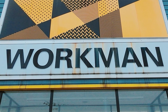 The image shows the exterior of a building with a large sign that reads &ldquo;WORKMAN.&rdquo; The sign has a geometric pattern above the text