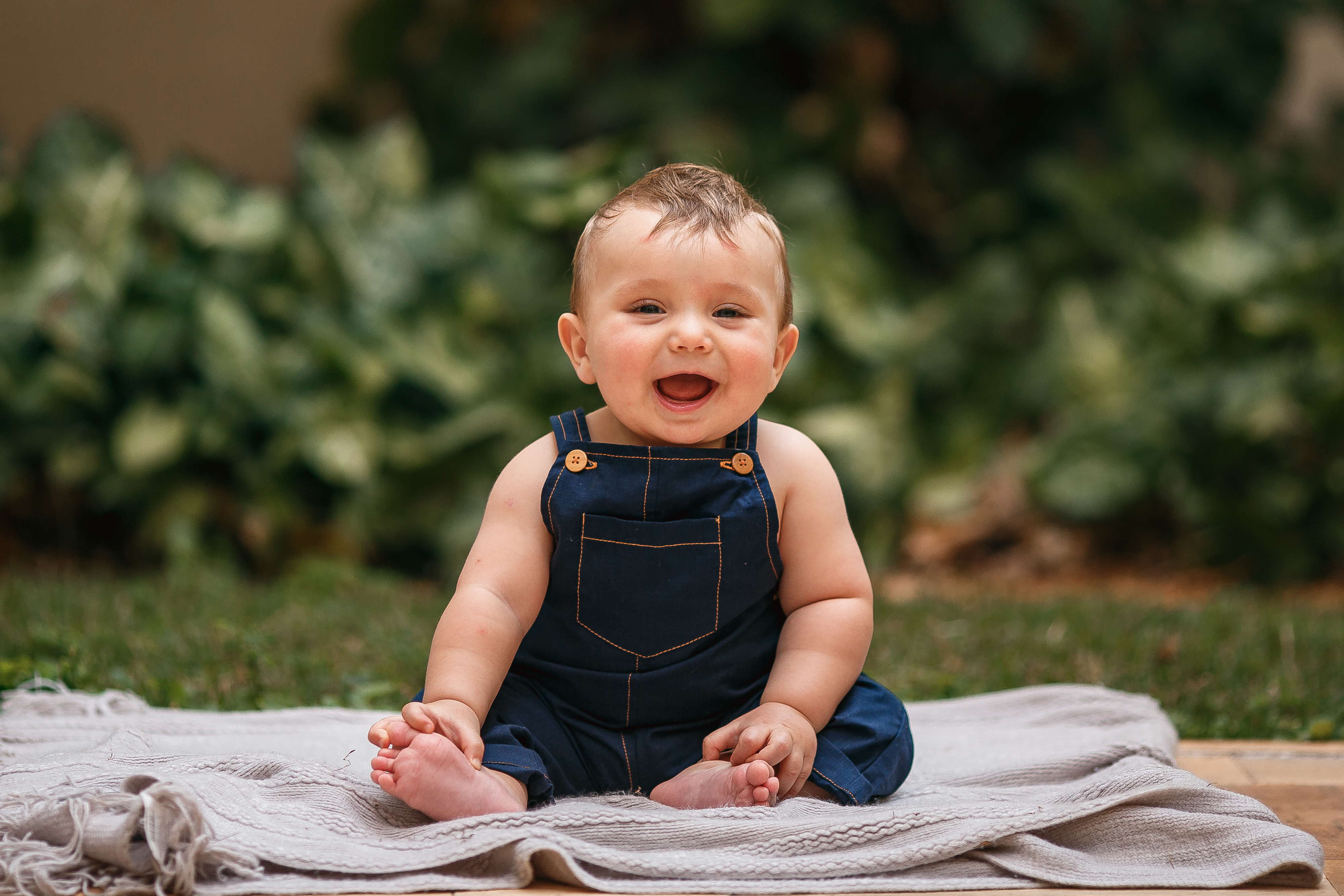 A smiling baby sitting on a blanket outdoors