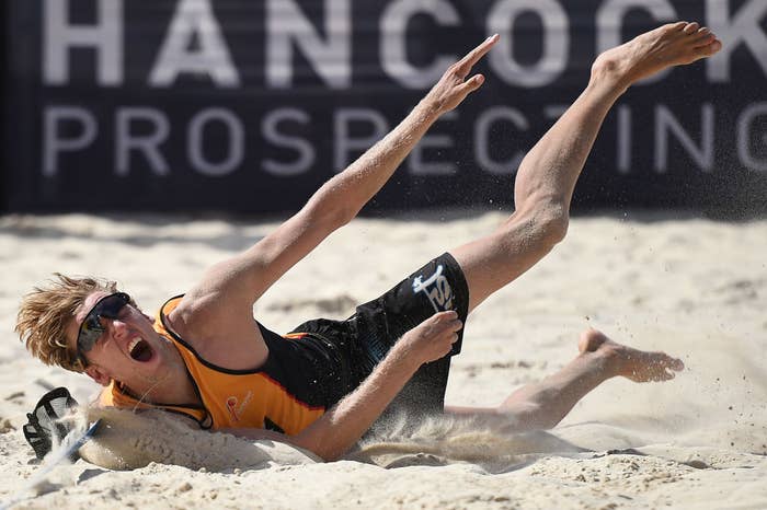 Beach volleyball player Zach dives in the sand to make a play during a match