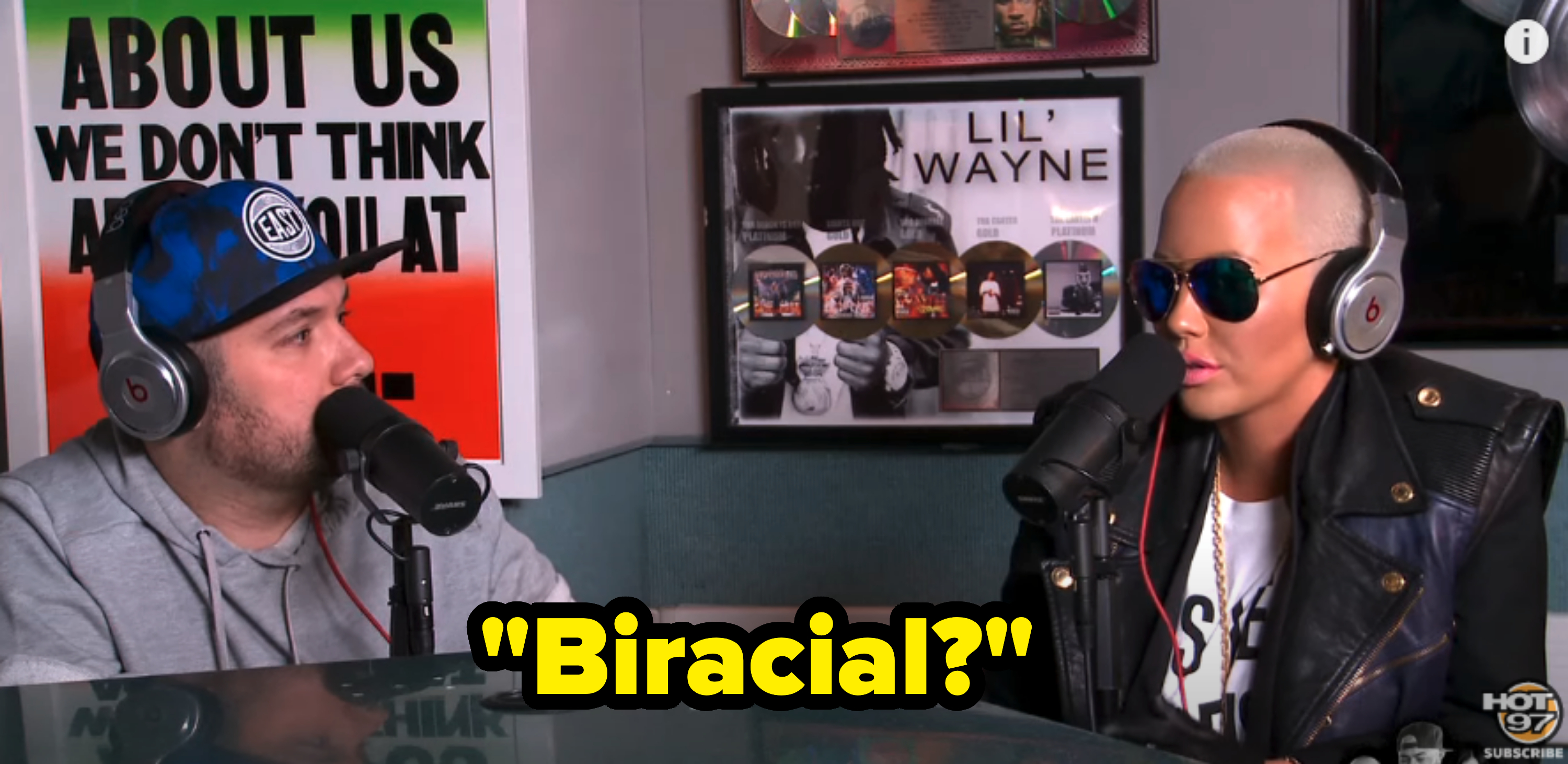 Amber Rose and a man having a conversation during a radio interview at Hot 97, with a framed Lil' Wayne poster in the background