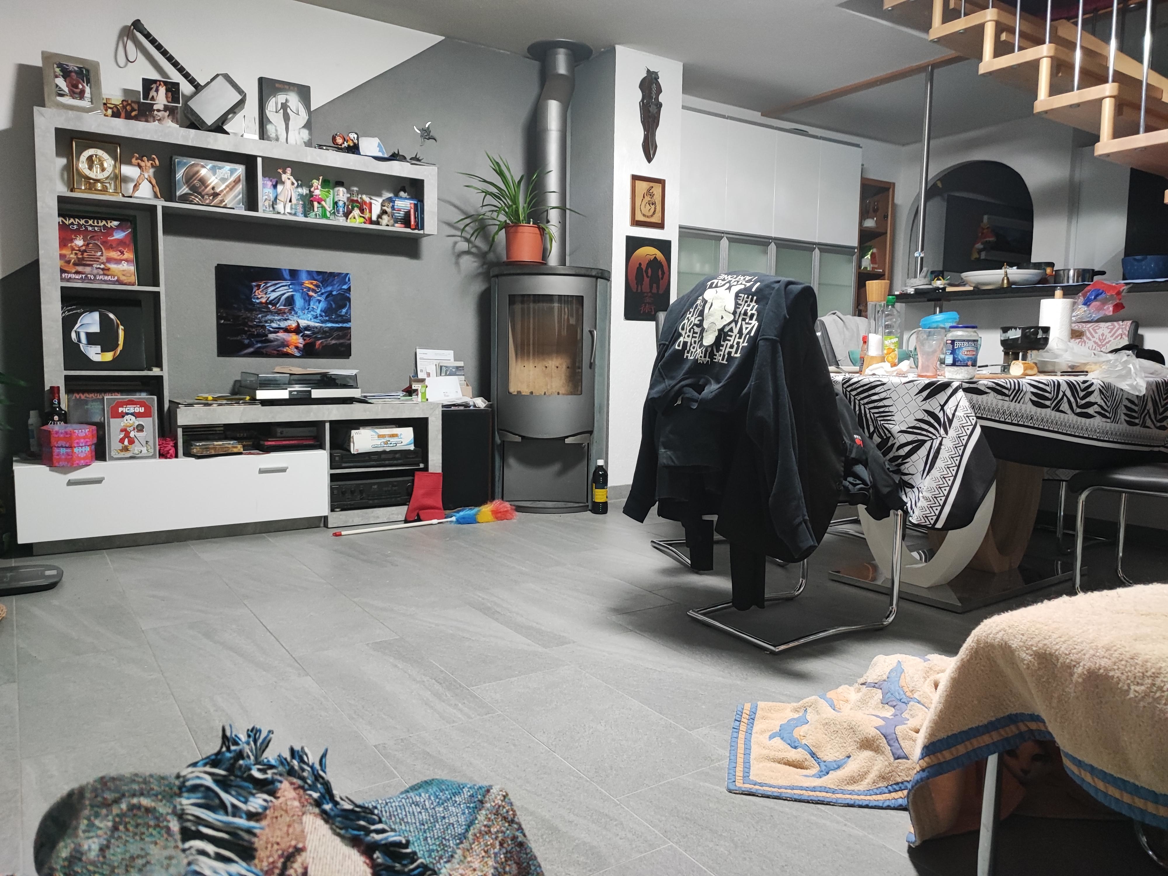 Living room with modern amenities, including a TV, a fireplace, shelves with various decorations, a dining table with chairs, and an overhead staircase